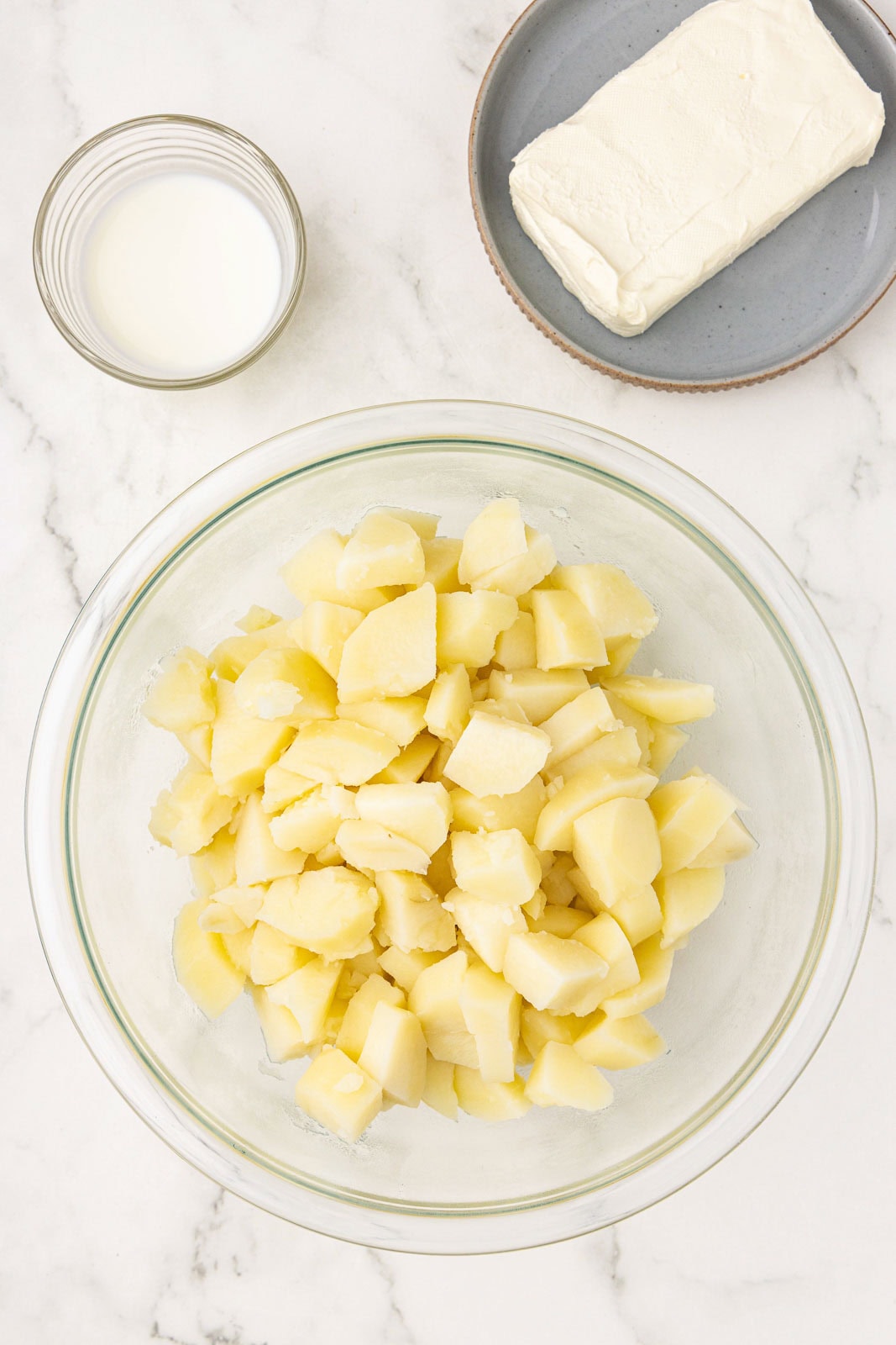 clear bowl of cooked potatoes and butter, with milk and cream cheese on side