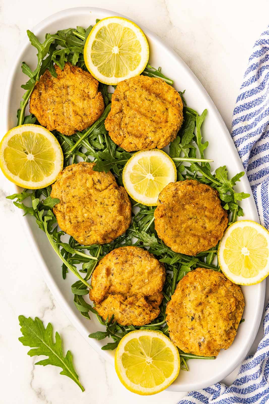 large white platter with air fried salmon patties on a bed of arugula with slices of lemon