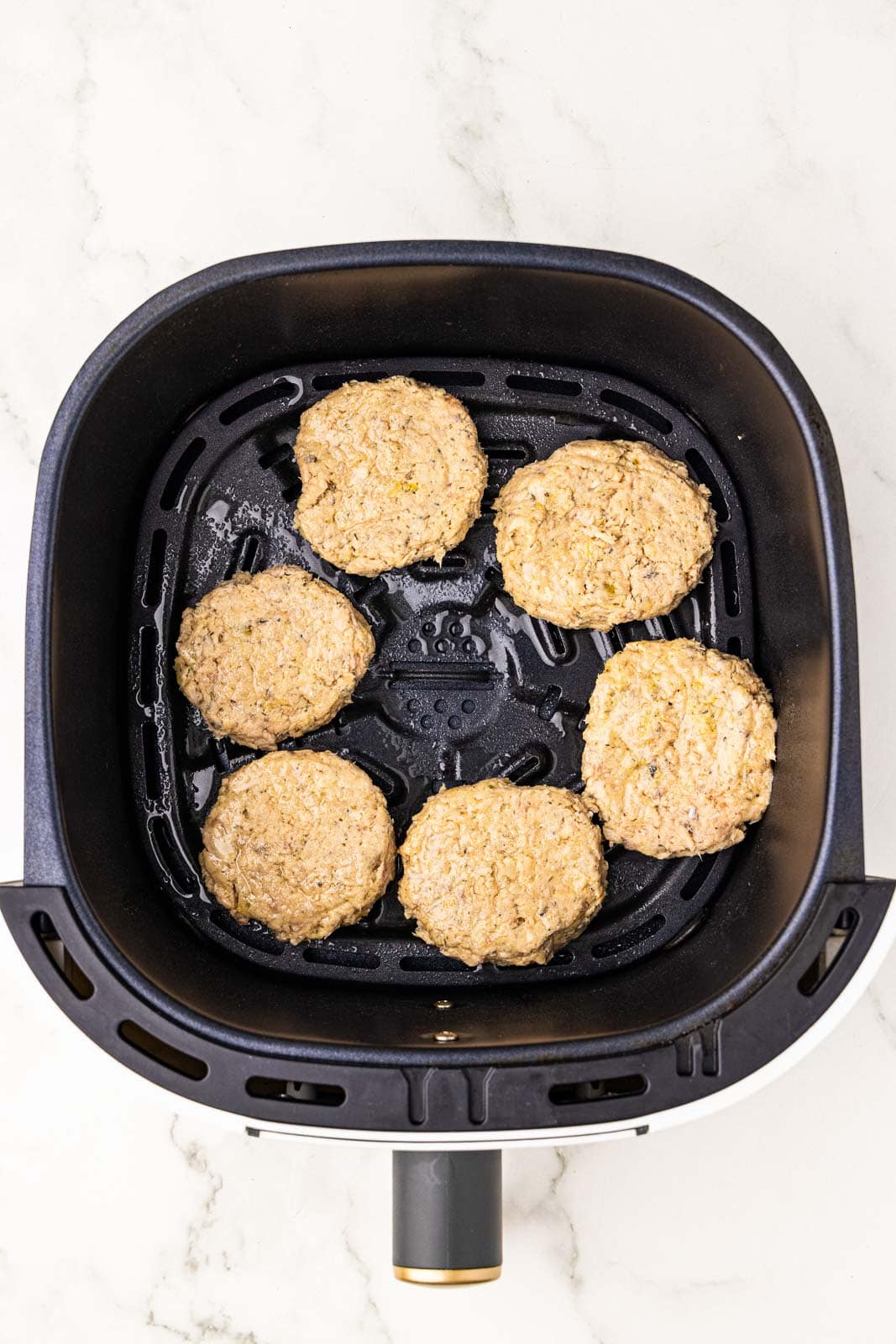 overhead view of black air fryer with six salmon patties that have been sprayed with avocado oil