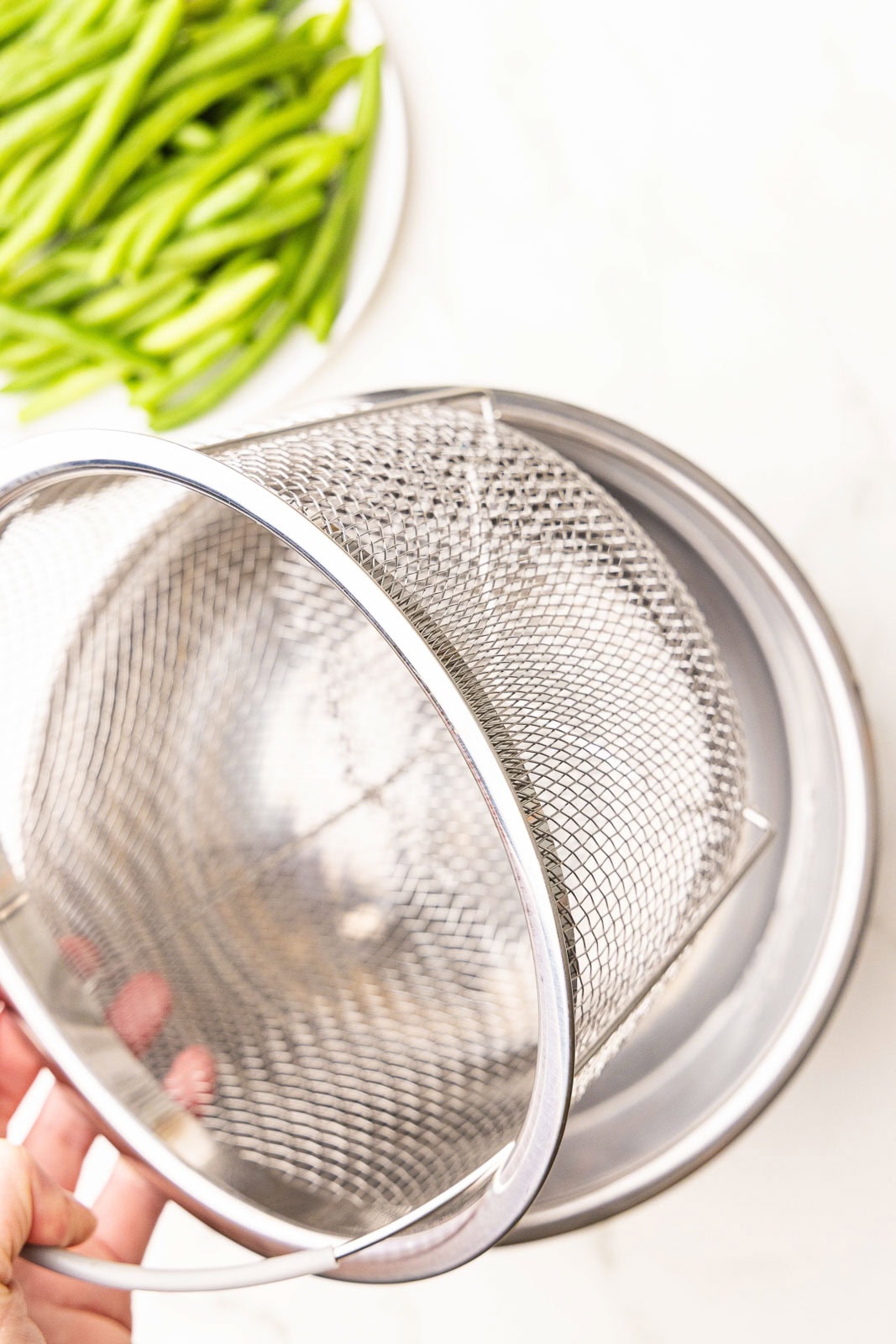 overhead view of instant pot steamer basket with plate of fresh green beans in background