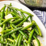 closeup view of white platter containing cooked green beans with pats of butter with salt container and instant pot in background