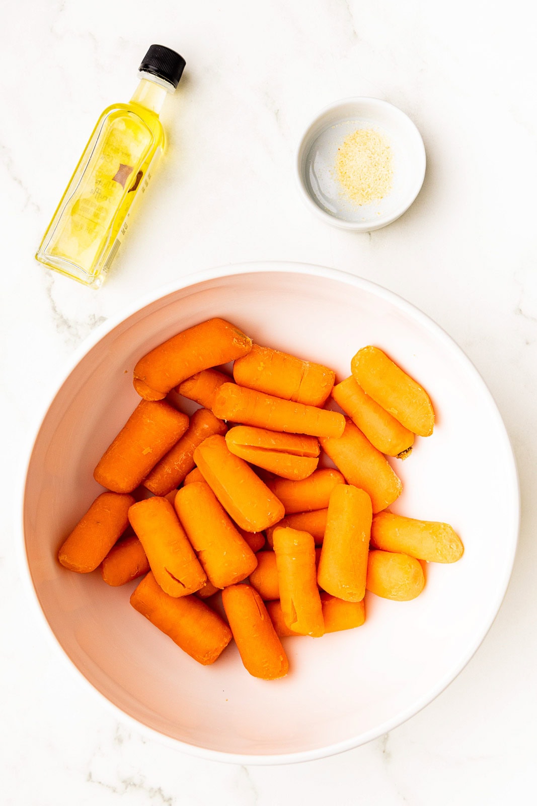 large bowl of baby carrots with small bowl of garlic powder and container of olive oil on side