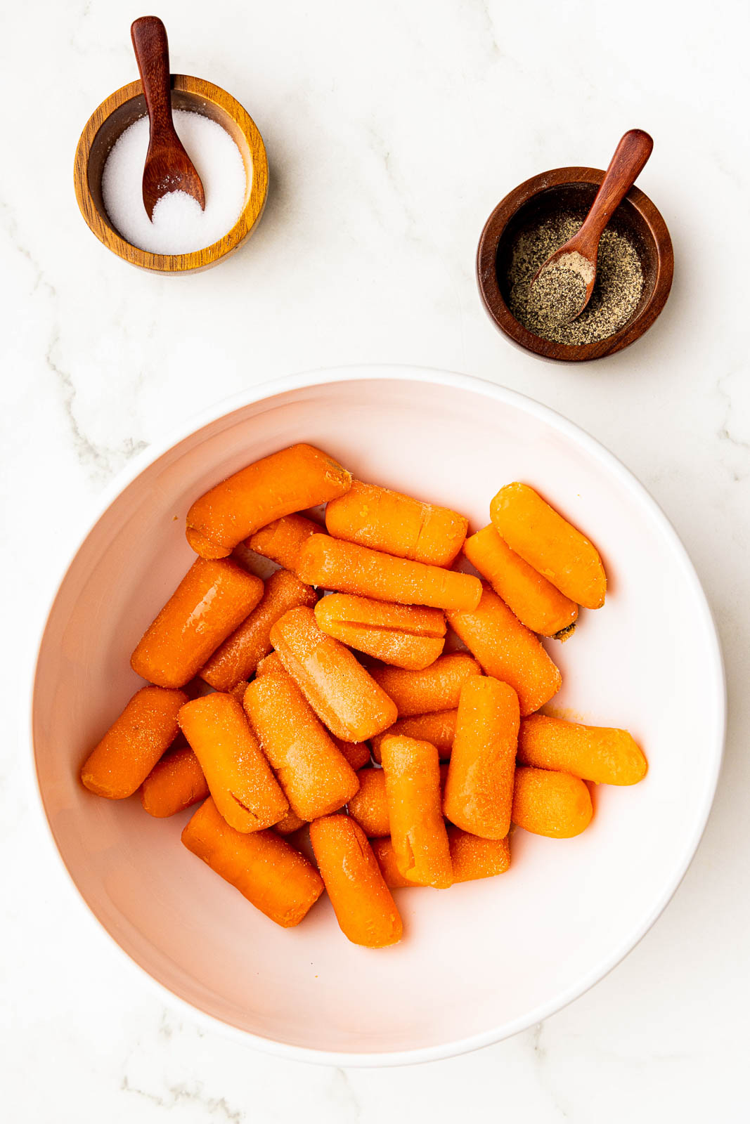 overhead view of white bowl of baby carrots with bowls of salt and pepper on side