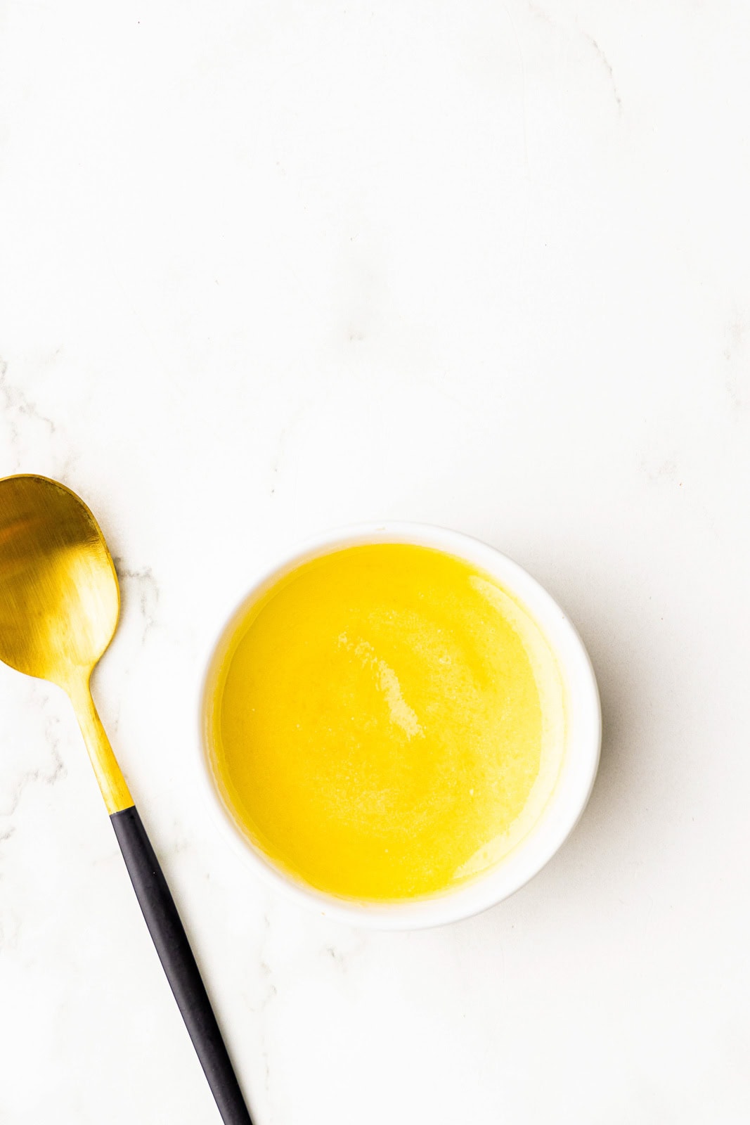 small bowl of melted butter and honey with gold spoons on side