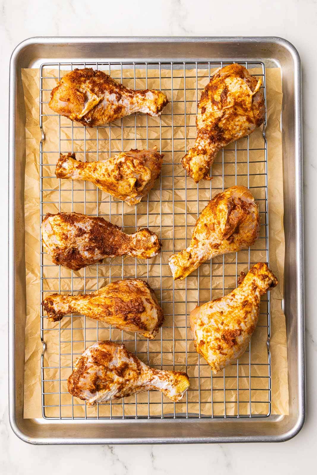 overhead view of chicken drumsticks on baking sheet and rack lined with parchment paper