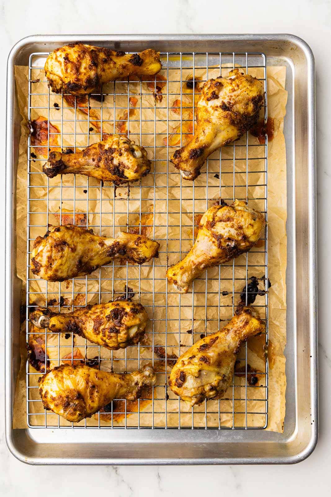 overhead view of baked chicken drumsticks on baking sheet and rack lined with parchment paper