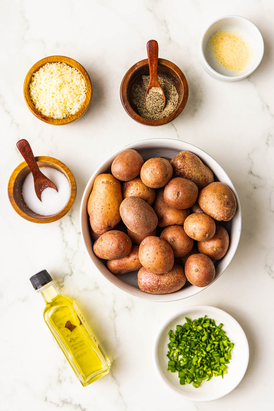 ingredients to include large bowl of baby potatoes surrounded by containers of olive oil, salt, pepper, garlic powder, Parmesan cheese and chives