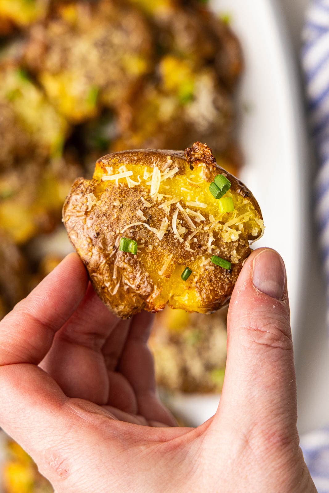 closeup view of hand holding smashed potato with platter of potatoes in the background