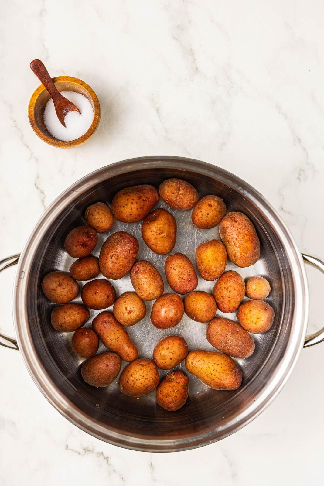 overhead view of water filled pot with potatoes with a container of salt on the side
