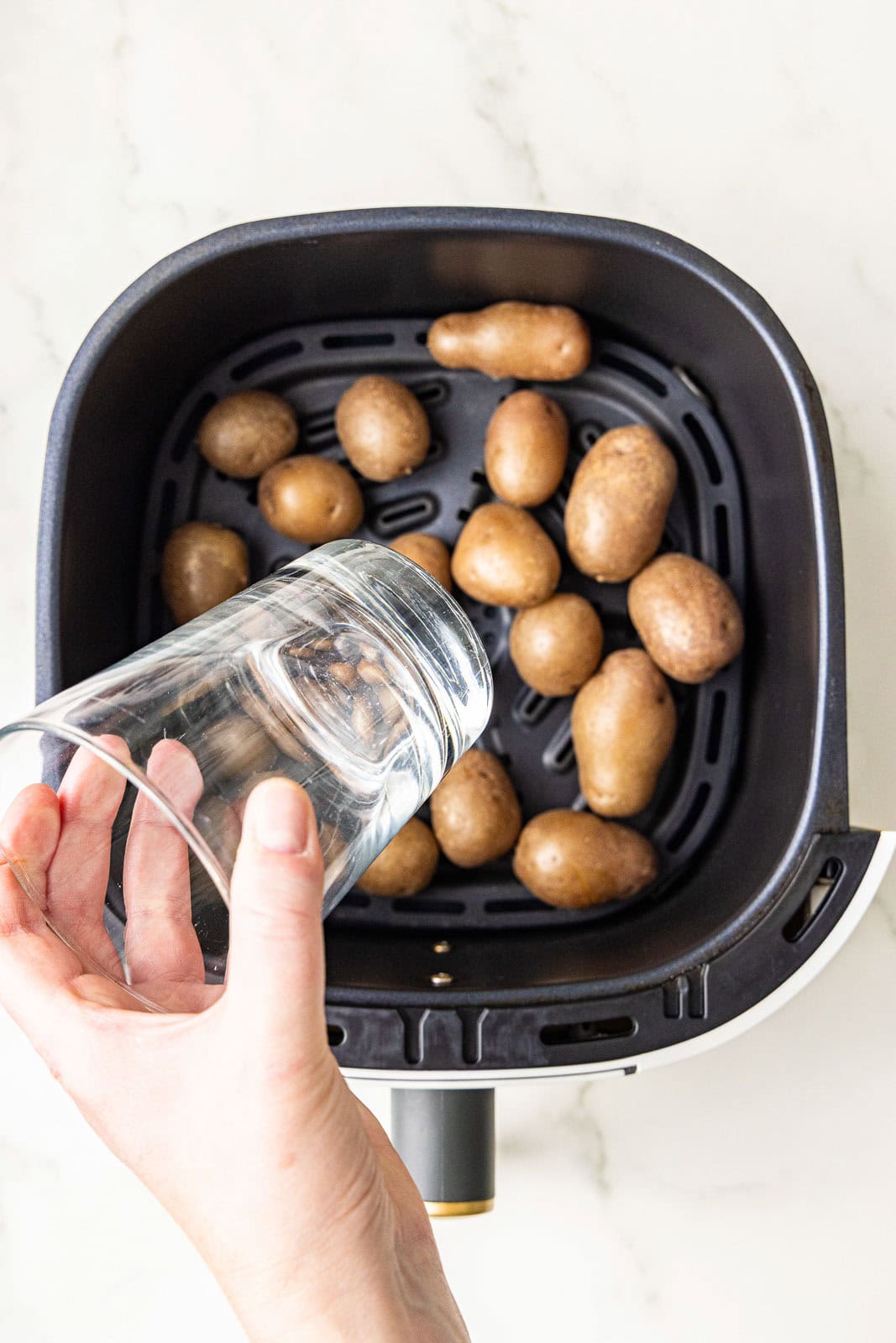 black air fryer with boiled potatoes and hand holding glass ready to smash potatoes