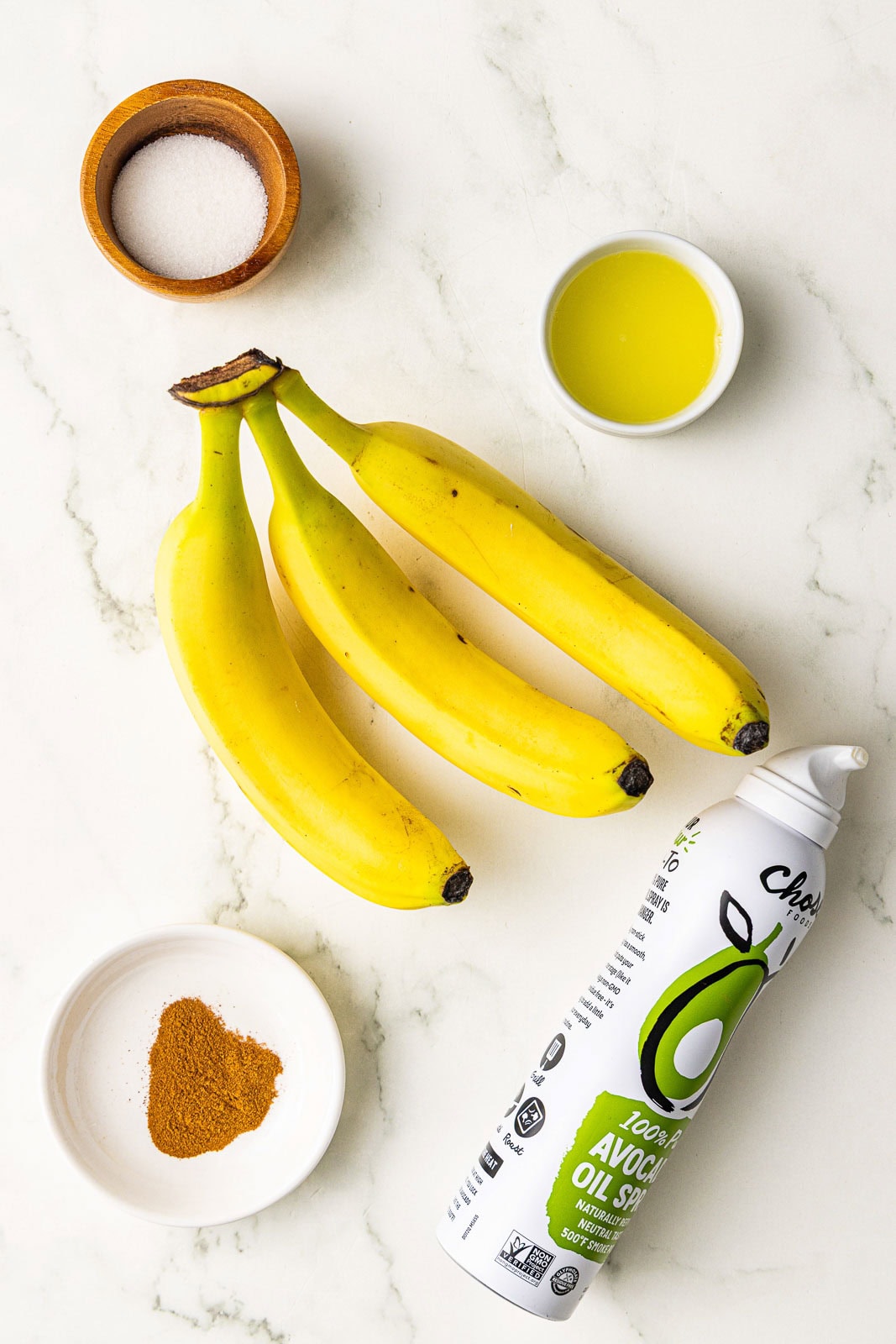 ingredients to include 3 bananas surrounded by containers of lemon juice, ground cinnamon, sugar and avocado oil