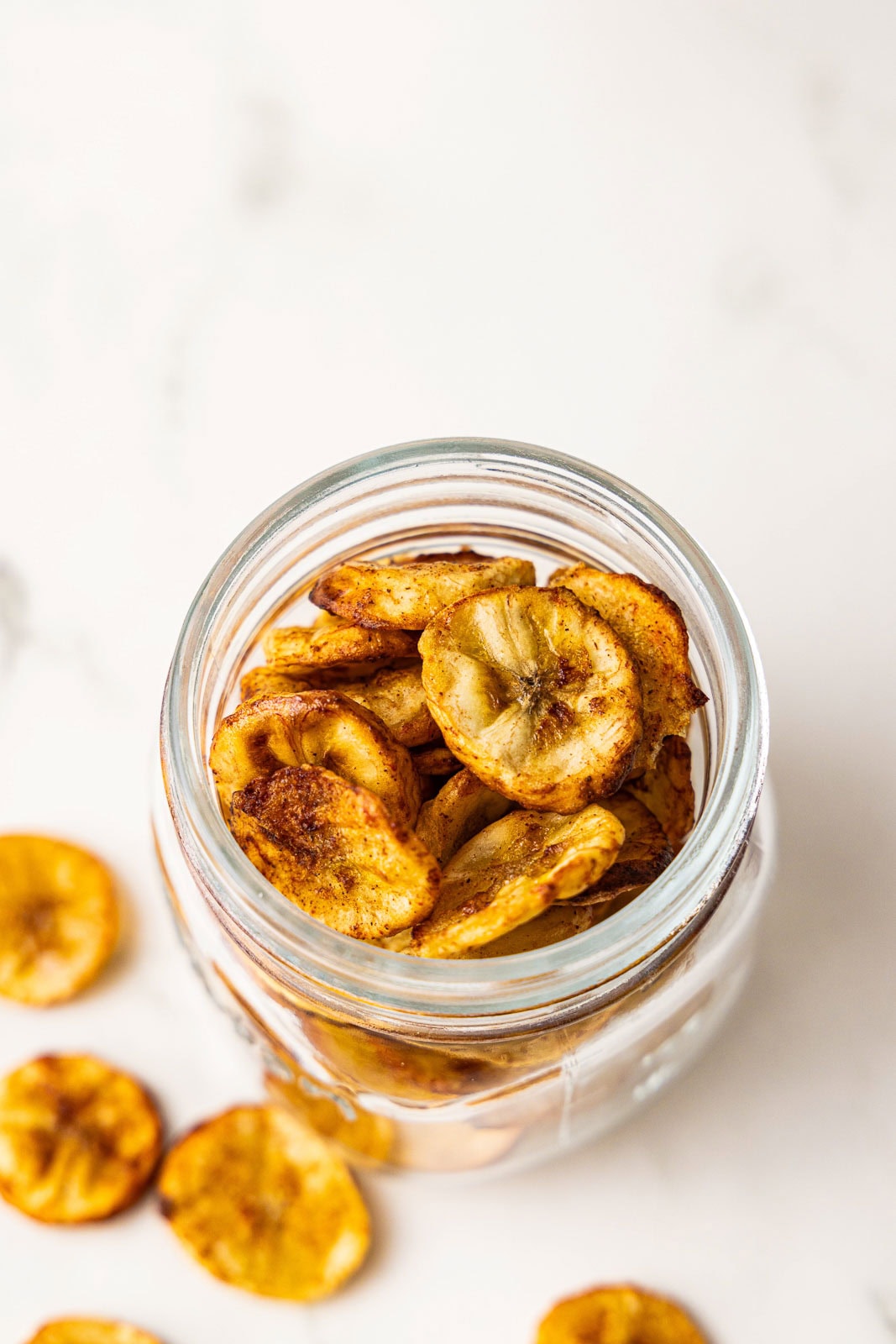 overhead view of glass jar containing banana chips with a few chips scattered below