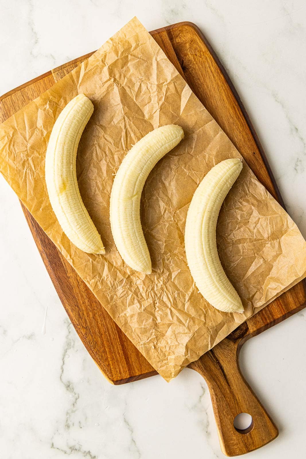 parchment lined wooden cutting board containing 3 peeled bananas