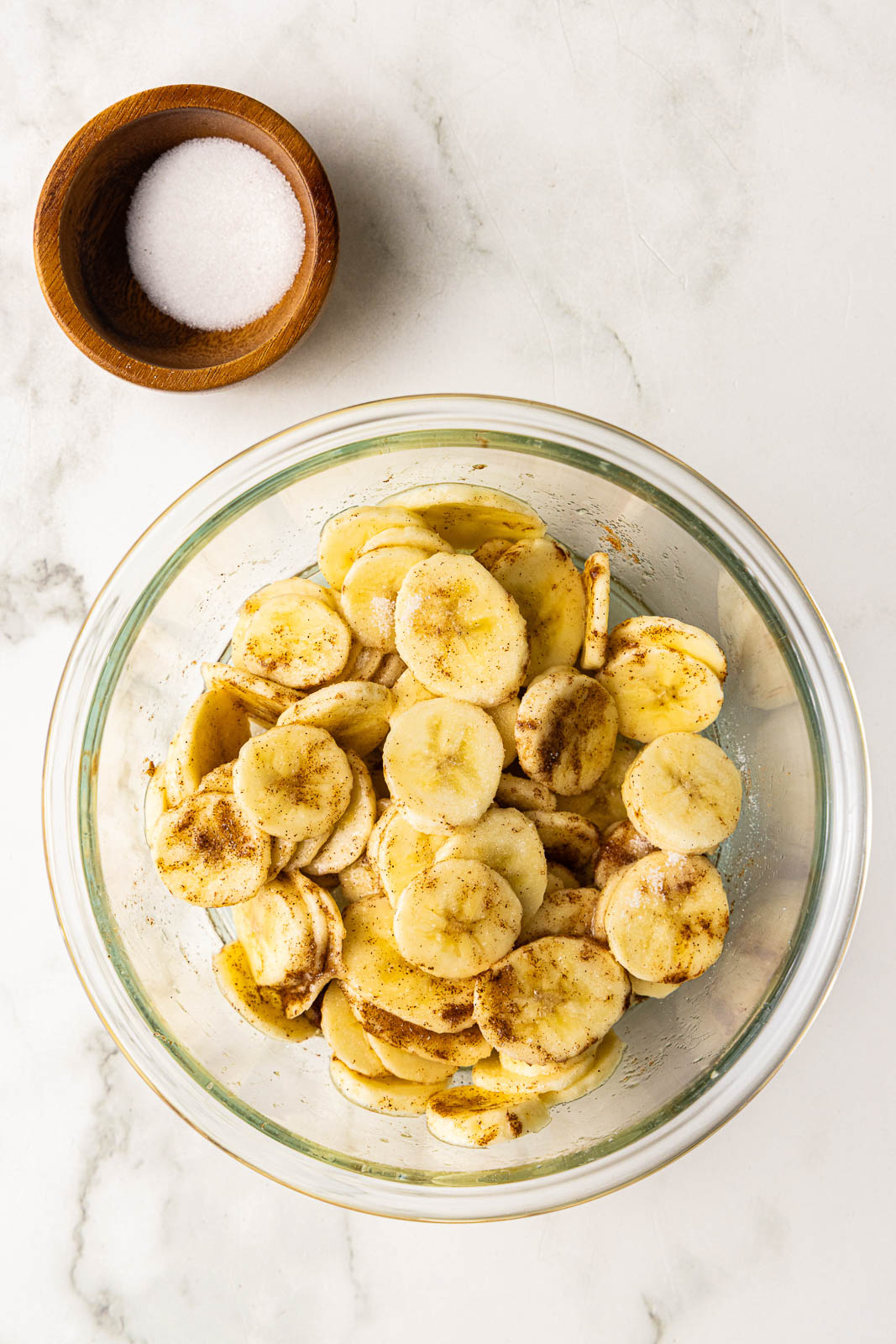bowl of sliced bananas that have been tossed with cinnamon with bowl of sugar on side