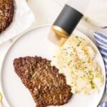 white dinner plate with 1 cube steak and mashed potatoes with air fryer and another cube steak in background