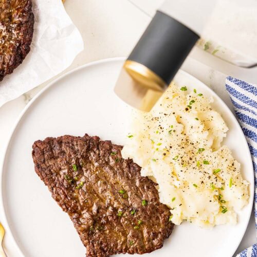 white dinner plate with 1 cube steak and mashed potatoes with air fryer and another cube steak in background