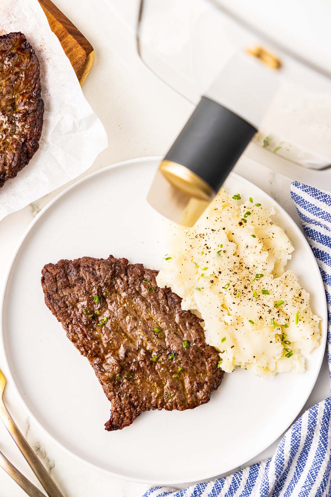 white dinner plate with 1 cube steak and mashed potatoes with air fryer and another cube steak in background