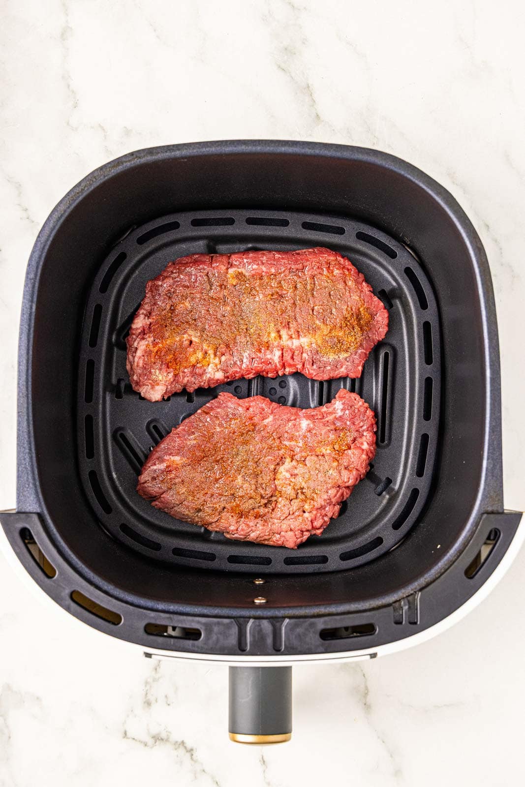 black air fryer containing 2 seasoned cube steaks