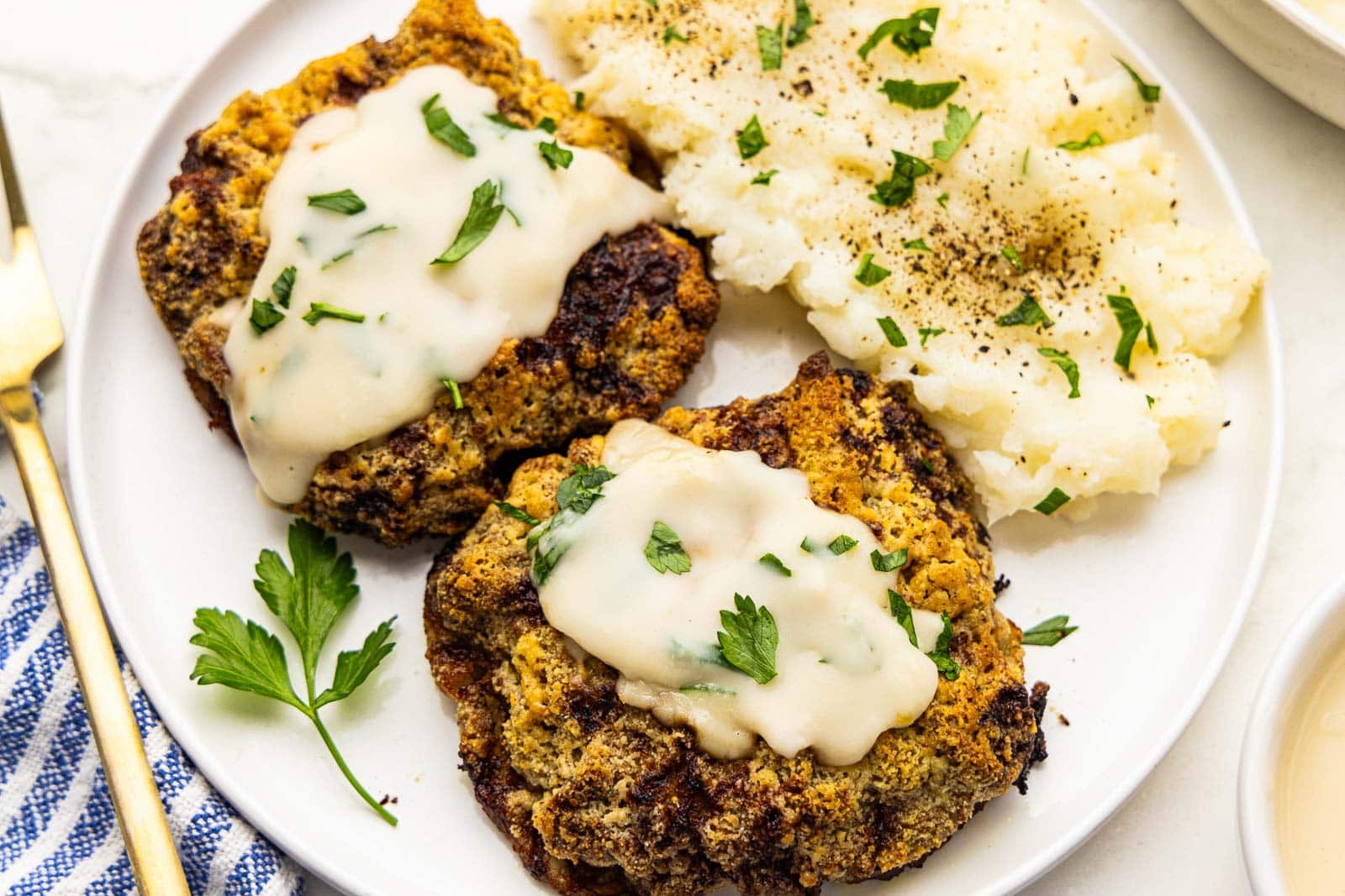 closeup view of 2 pieces of air fried cube steak with gravy on top and mashed potatoes with parsley, fork on the side