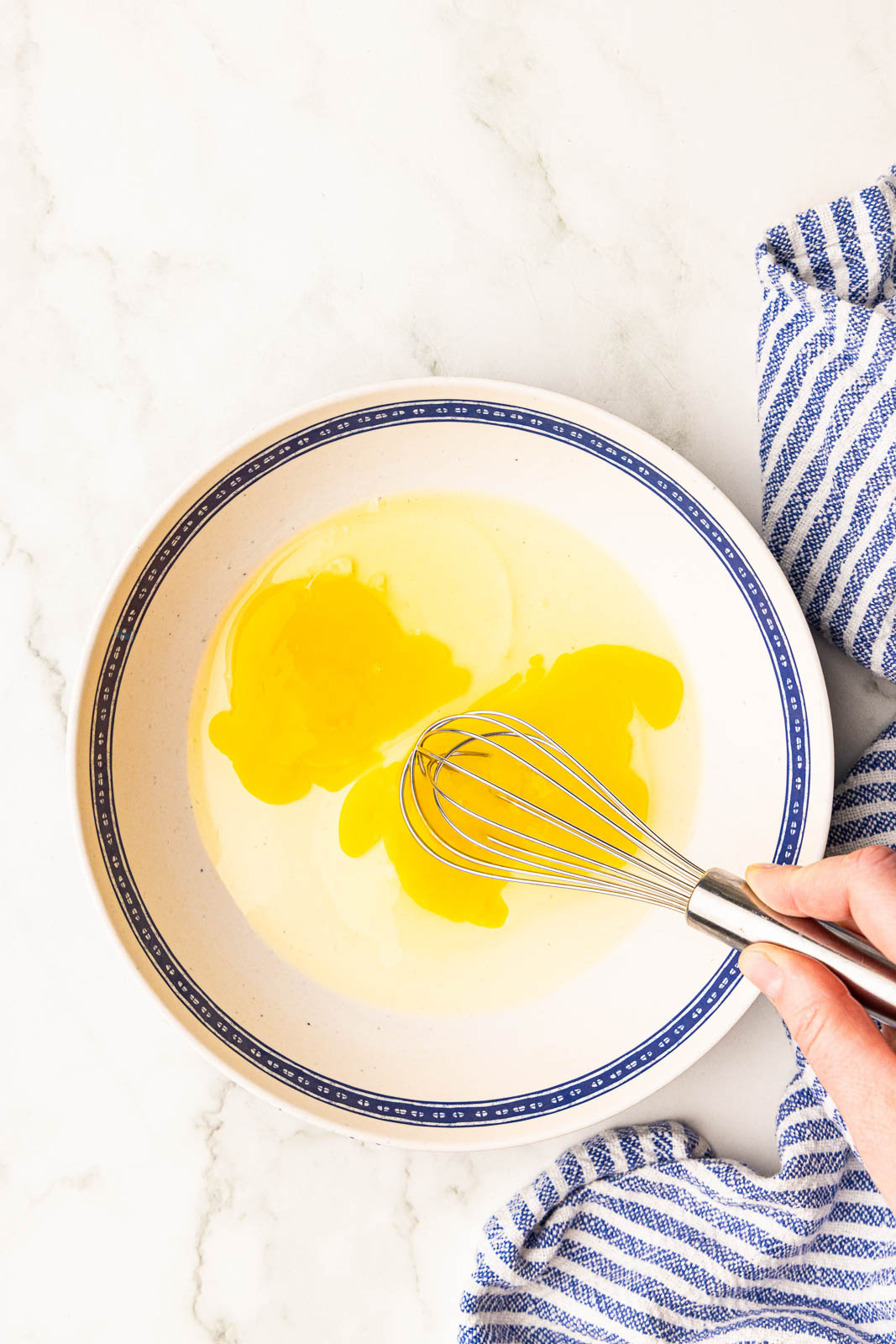 overhead view of large bowl of eggs being beaten with a hand holding a wire whisk