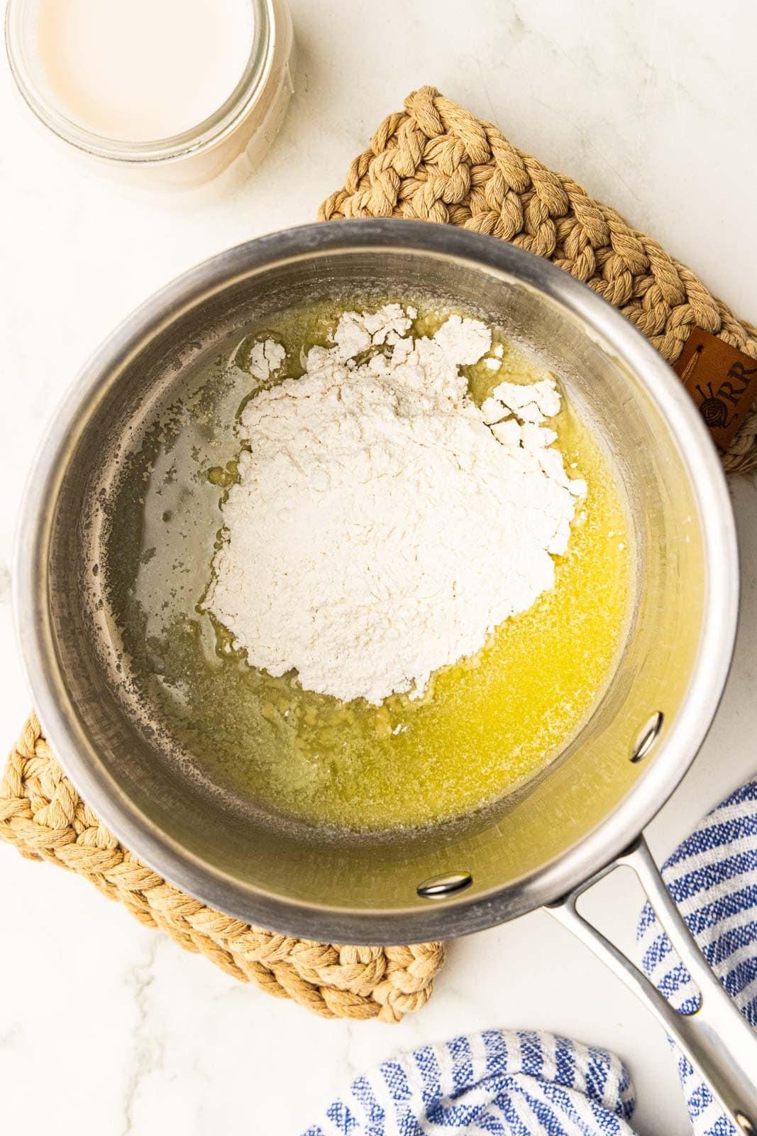 overhead view of sauce pan of melted butter and flour on mat with almond milk on the side