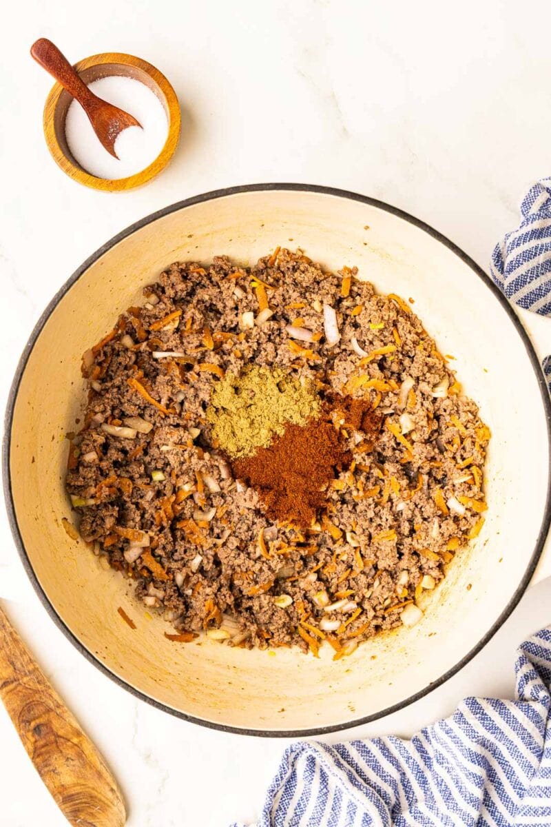 overhead view of Dutch oven with ground bison and seasonings with salt container on the side