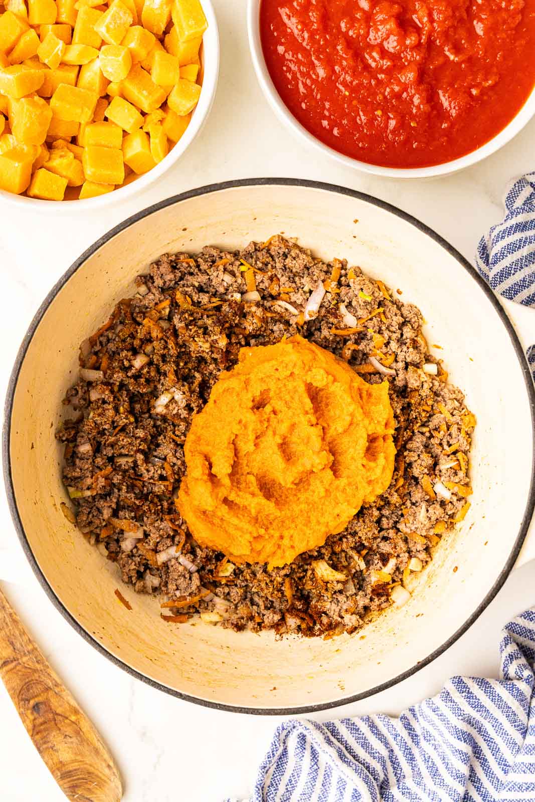dutch oven with ground bison mix and pumpkin, with containers of crushed tomatoes and butternut squash on side
