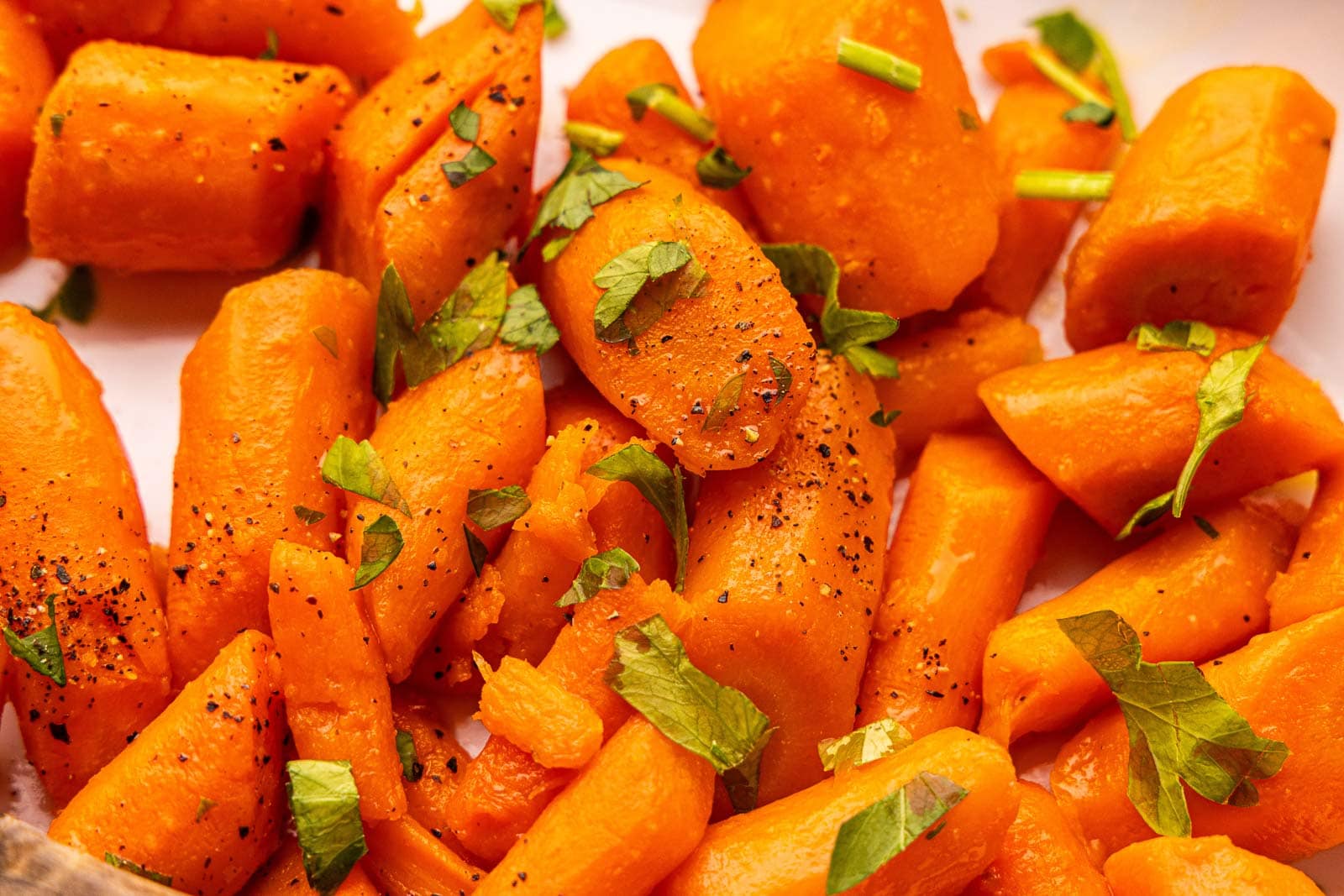 closeup view of cooked carrots sprinkled with parsley and seasoned with pepper