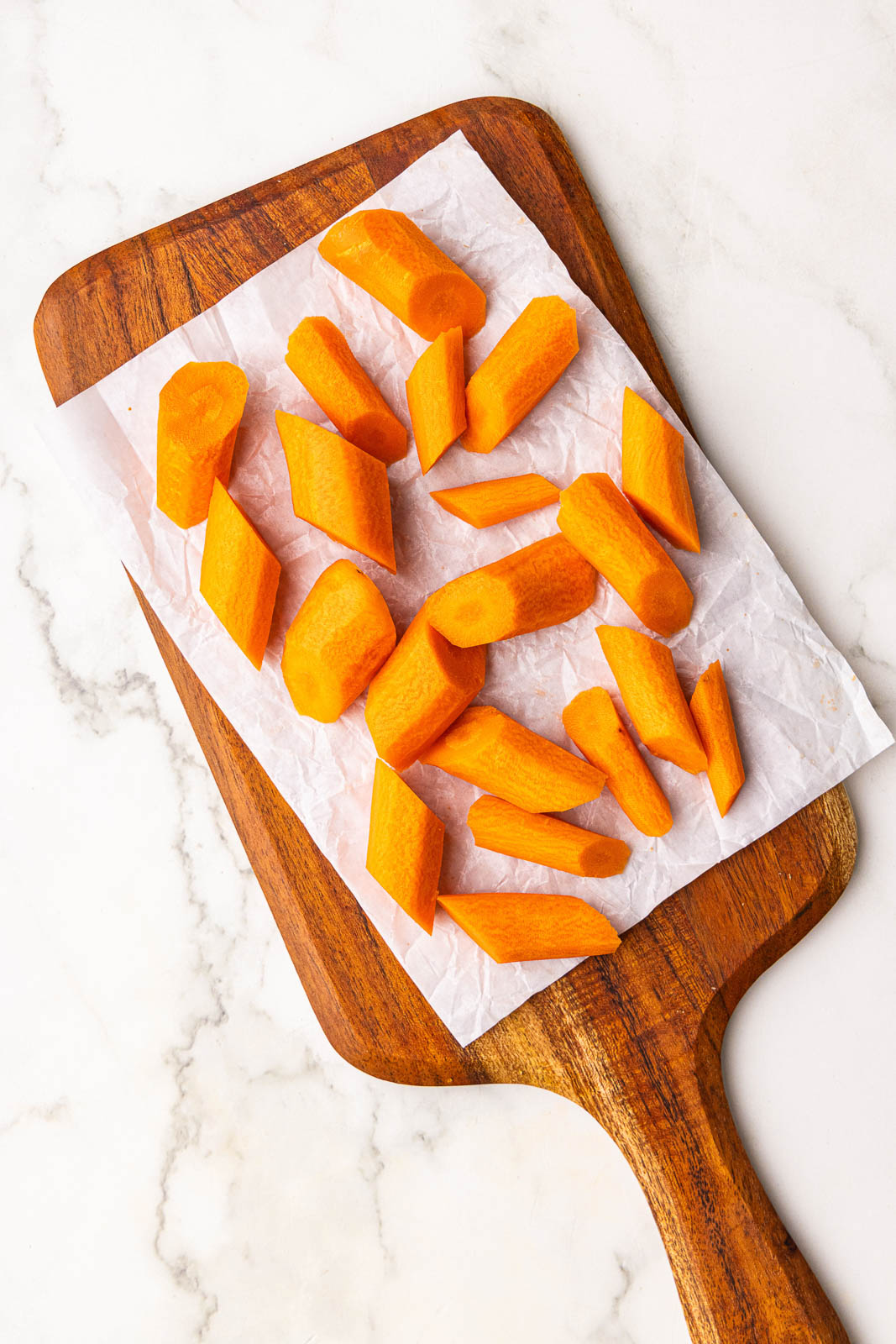 parchment lined wooden cutting board with peeled and wedged carrots