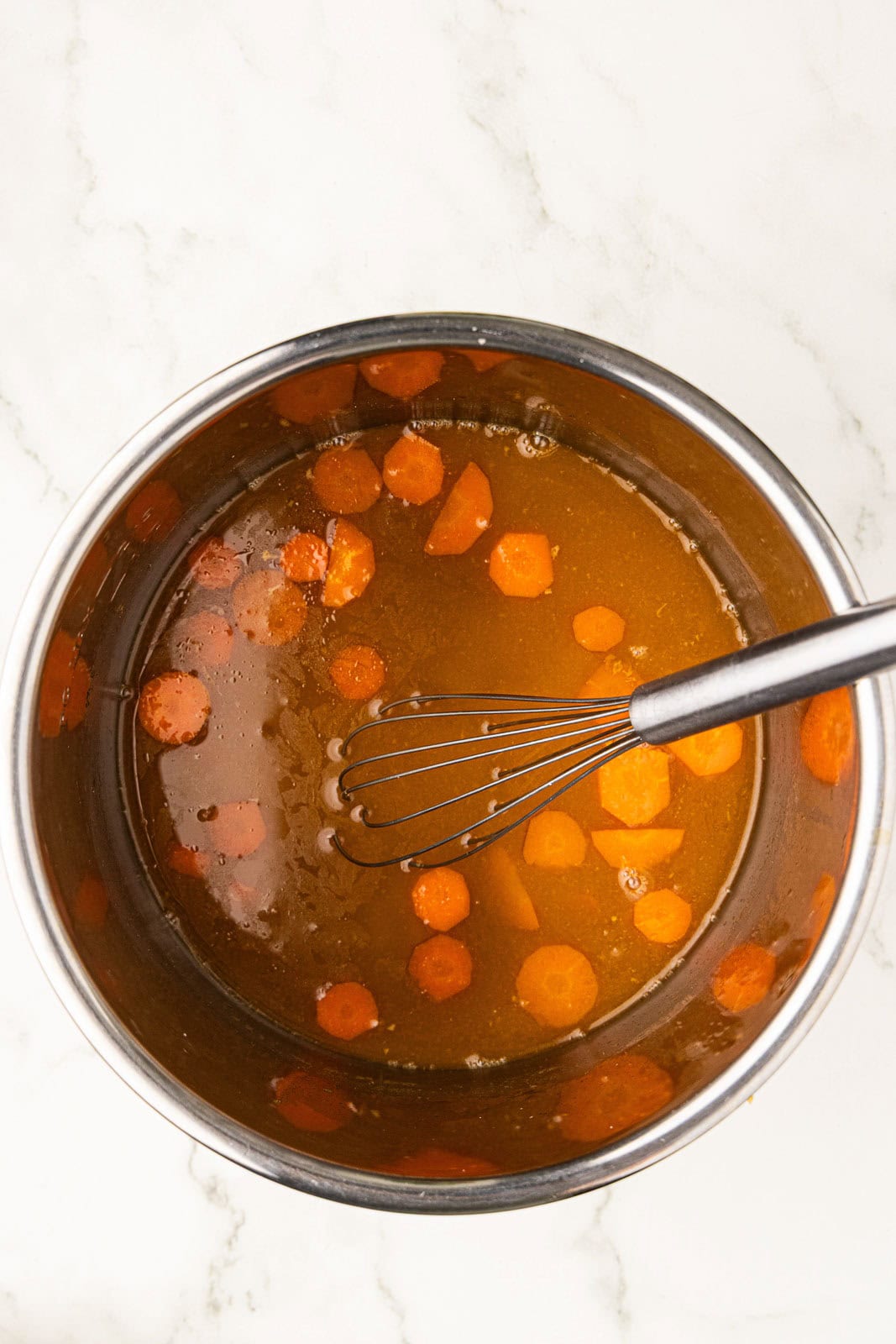 instant pot bowl with liquid and cooked carrots with wire whisk inside