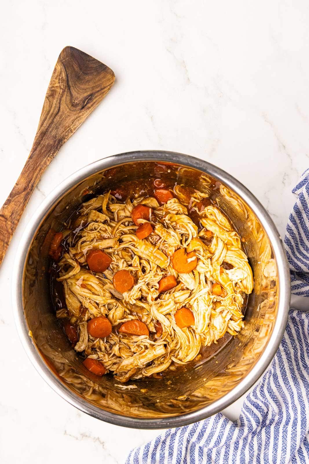 instant pot bowl of shredded chicken, juice and carrots with wooden spatula on side