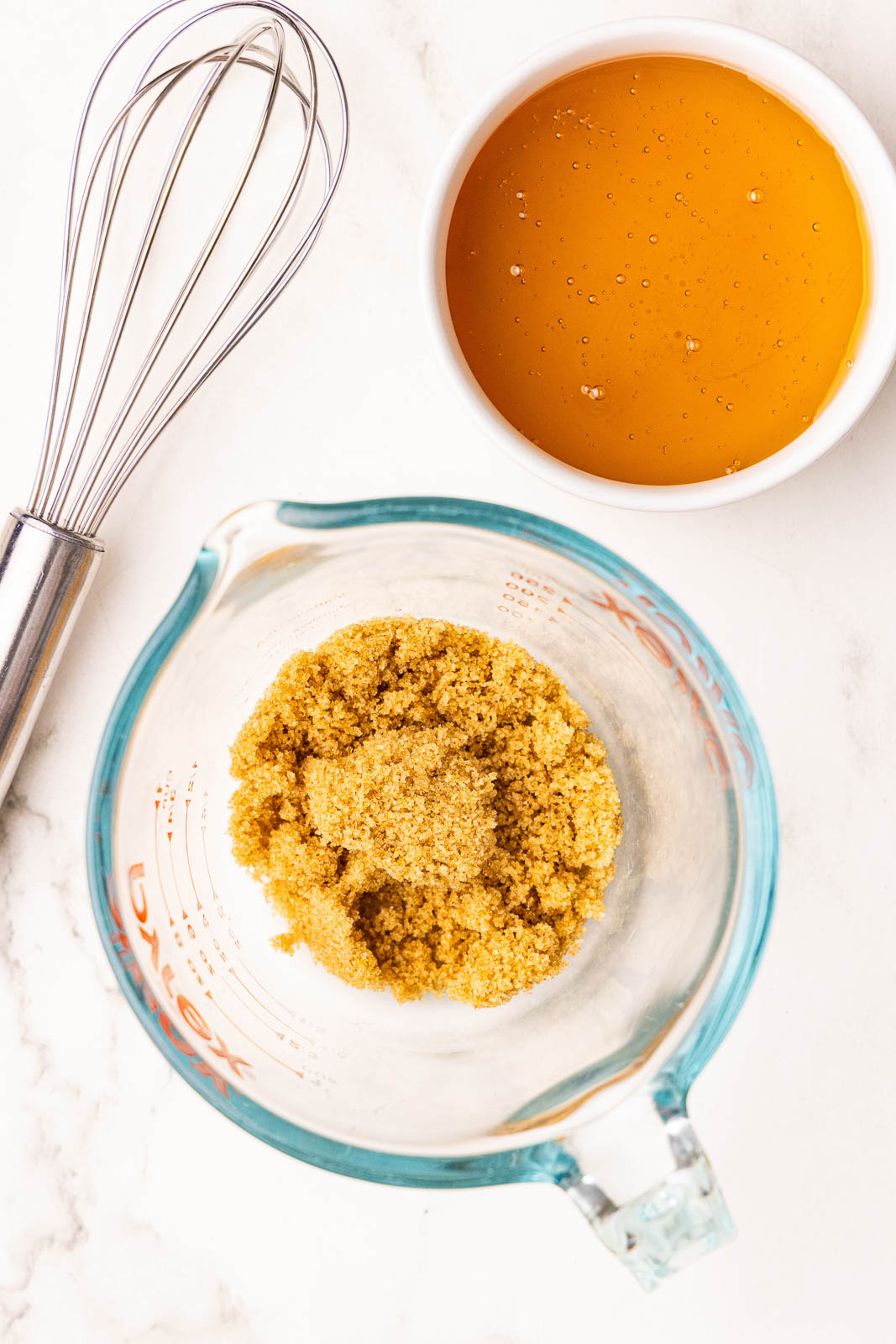 glass measuring cup with brown sugar and bowl containing honey with metal whisk on side