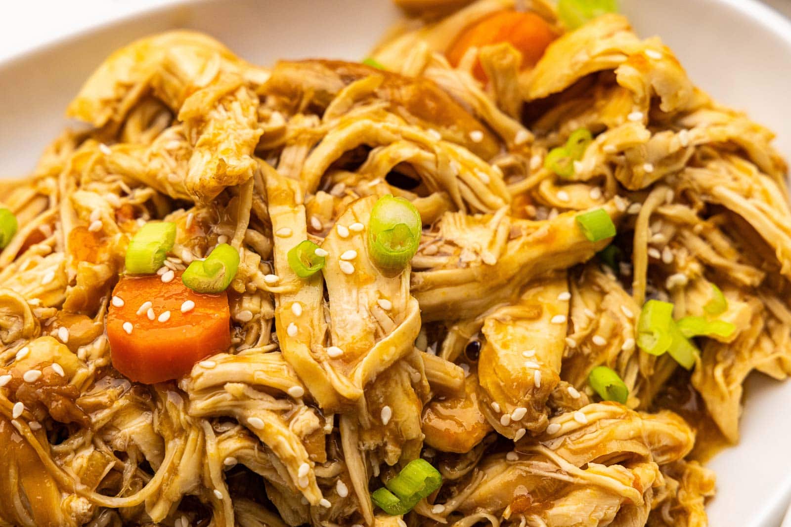 closeup of chicken and carrots on white platter, garnished with scallions and sesame seeds