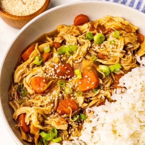 overhead view of chicken and carrots garnished with scallions and sesame seeds with rice with bowls of scallions and sesame seeds on side