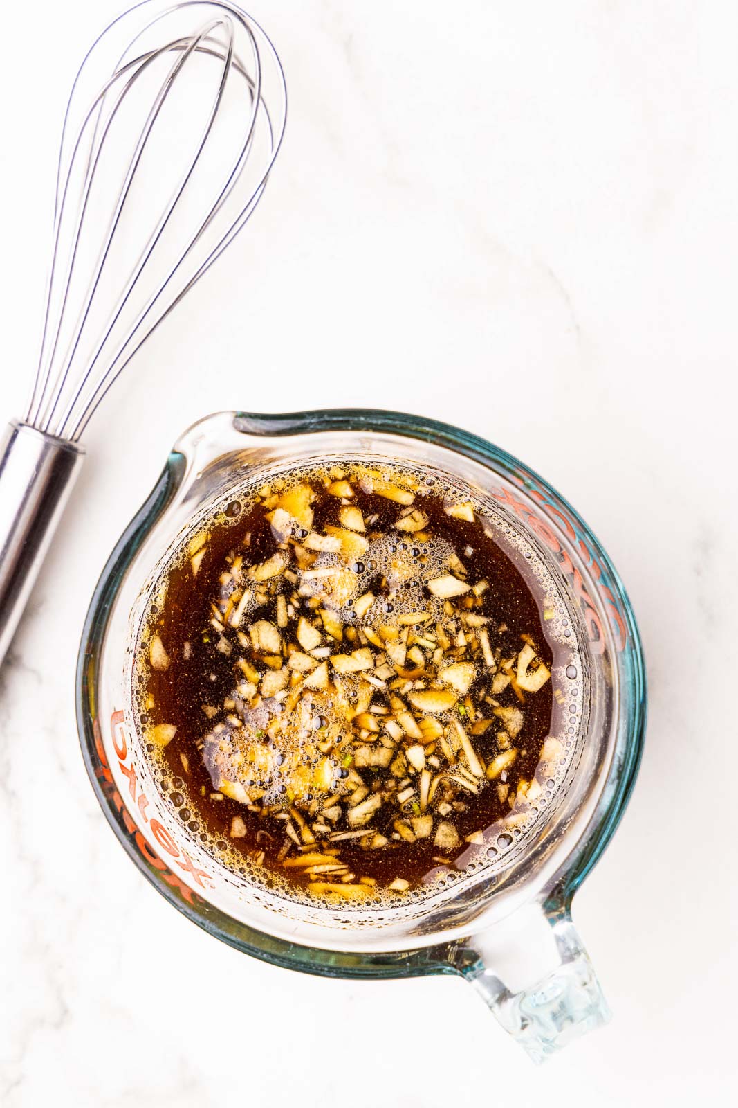 glass measuring cup with marinade ingredients with wire whisk on side