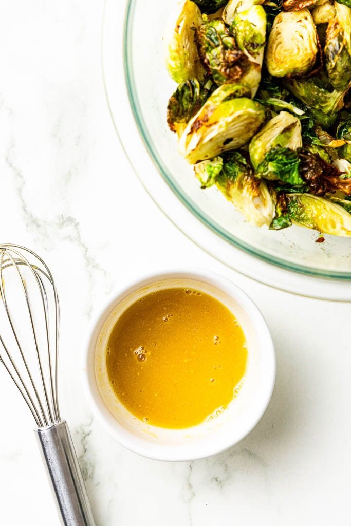 closeup of bowl of glaze, whisk and glass of air fried Brussels sprouts