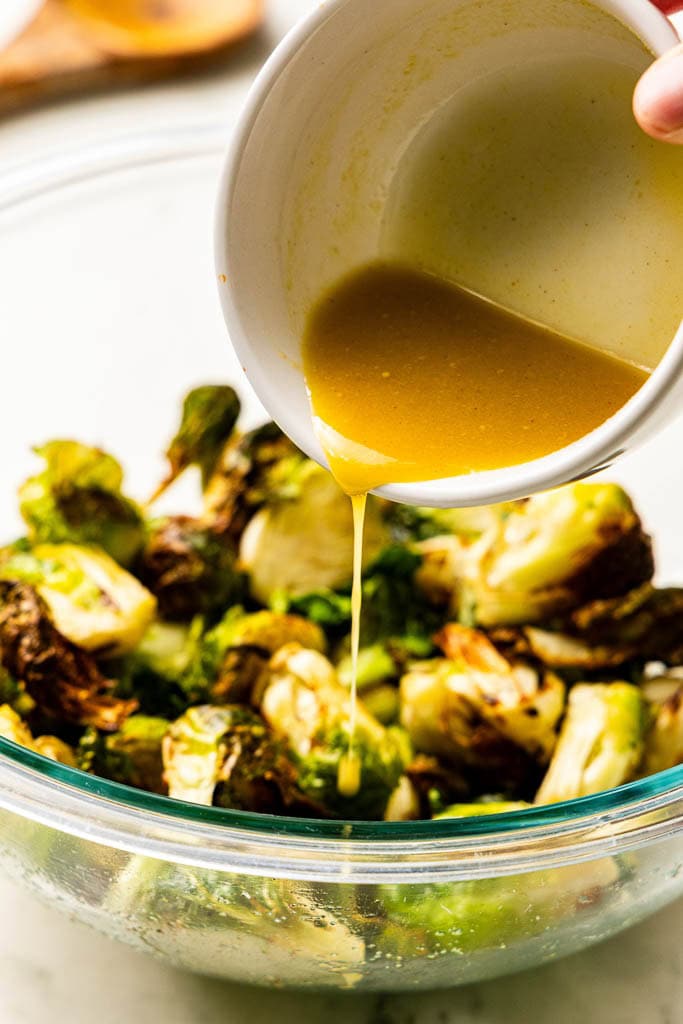 glass bowl of air fried Brussels sprouts with hand pouring glaze mixture over Brussels sprouts
