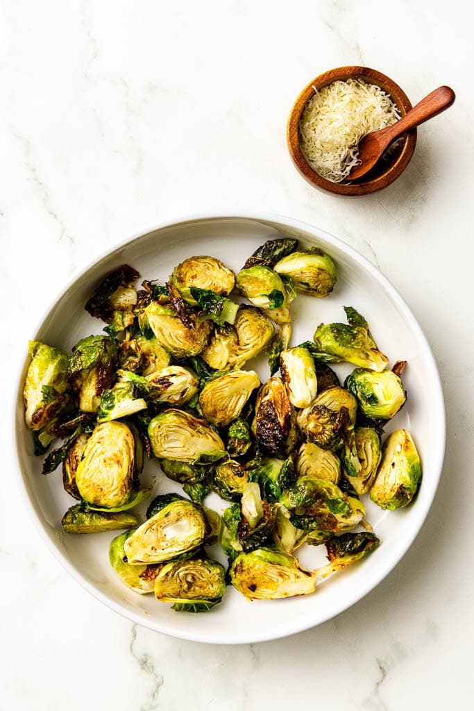 overhead view of air fried Brussels sprouts with container of Parmesan cheese on side