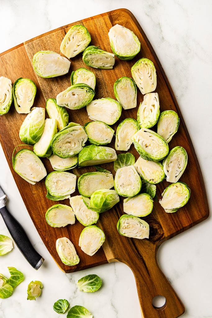 wooden cutting board with halved and trimmed Brussels sprouts with knife on side