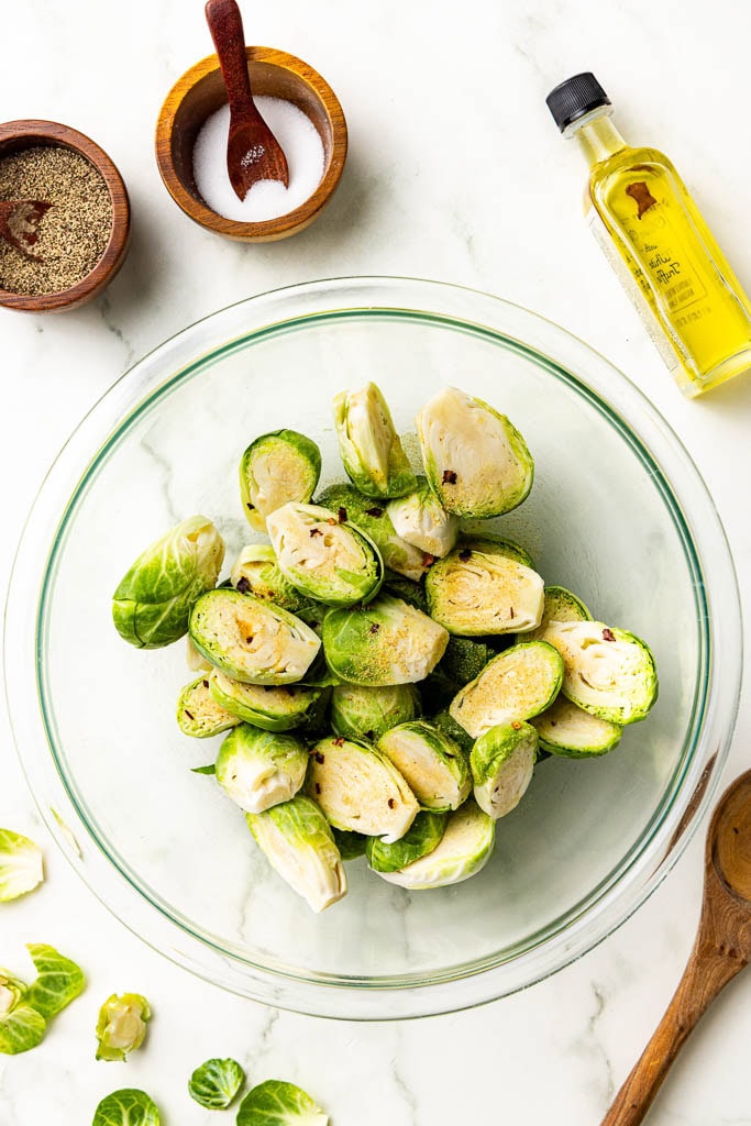 glass bowl of trimmed and halved seasoned Brussels sprouts with olive oil, salt and pepper on side