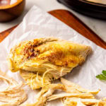 parchment lined wooden cutting board with partially chicken breast with salt and instant pot in background