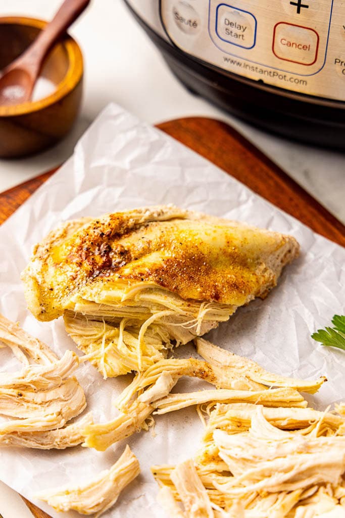 parchment lined wooden cutting board with partially chicken breast with salt and instant pot in background
