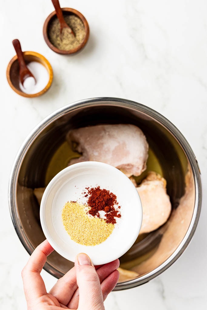 instant pot with chicken broth and chicken breasts with hand holding seasonings over instant pot, with salt and pepper in background