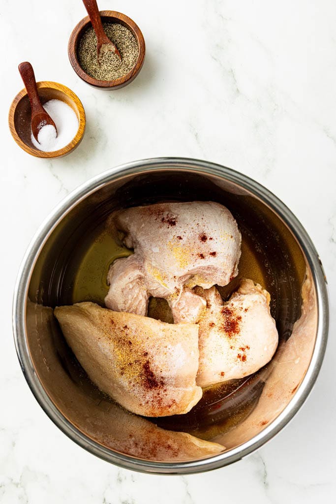 instant pot with seasoned chicken breasts in chicken broth with salt and pepper in background