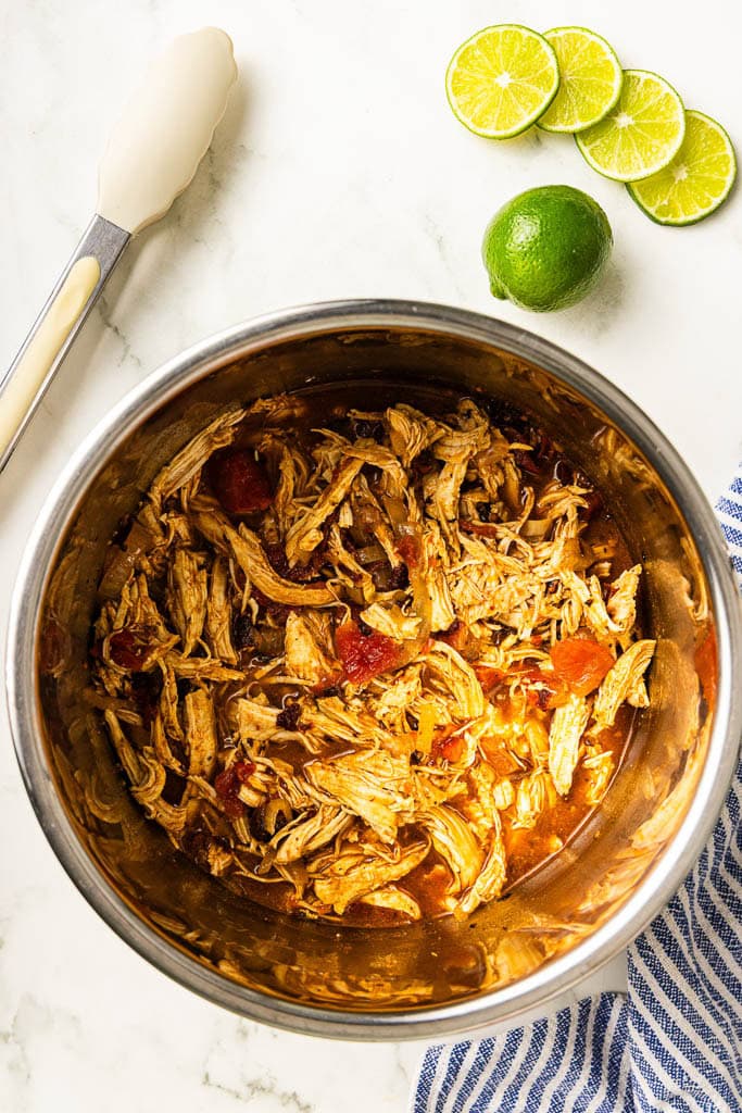 cooked instant pot chicken mixture with veggies, with tongs and sliced limes on side