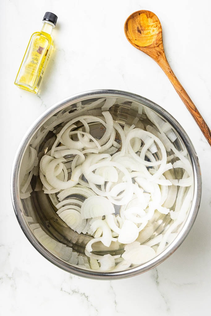 overhead view of instant pot with onion with olive and wooden spoon on side