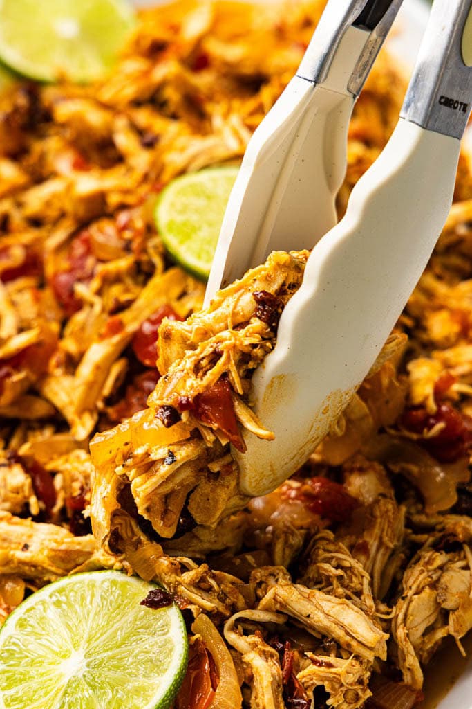 closeup of chicken tinga and lime slices, with white tongs