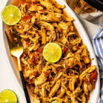 overhead view of white platter of chicken tinga with lime slices and gold fork, with instant pot in background