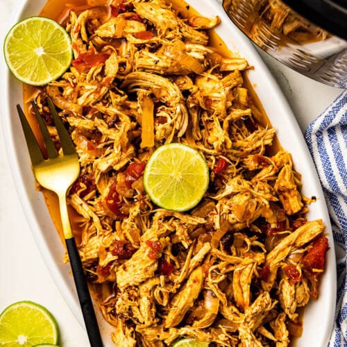overhead view of white platter of chicken tinga with lime slices and gold fork, with instant pot in background