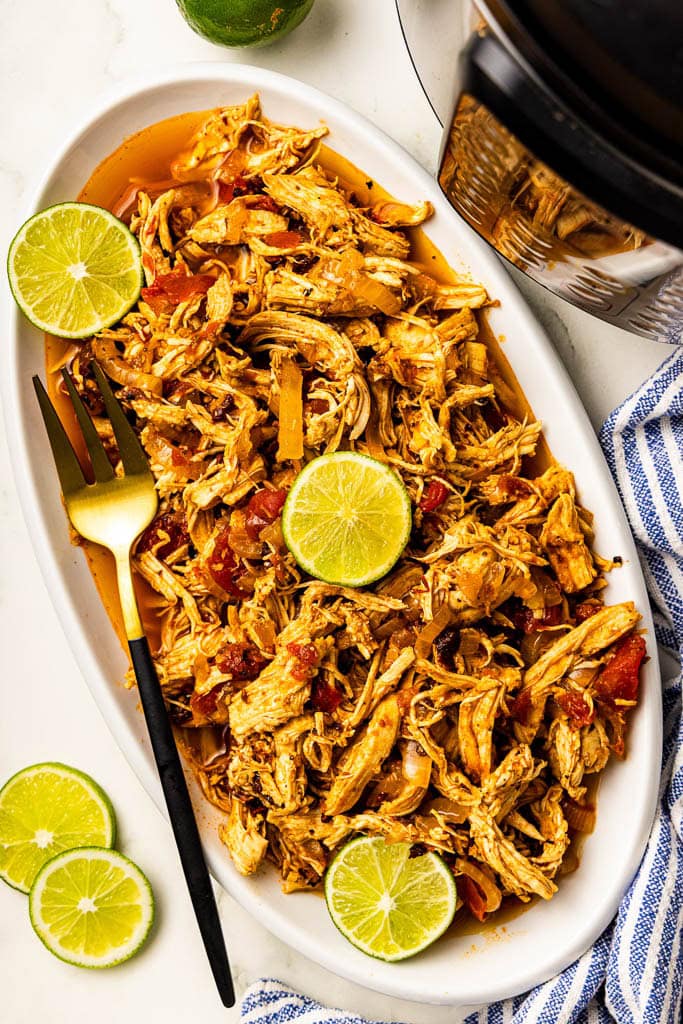 overhead view of white platter of chicken tinga with lime slices and gold fork, with instant pot in background